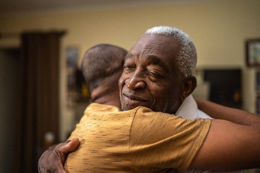An older man experiencing senior anxiety is comforted with a hug by his caregiver.